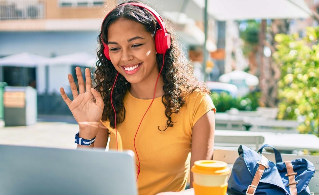 female college student sitting in front of computer waving at screen