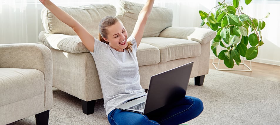 Triumphant high school student sitting at computer with arms raised after submitting college application’