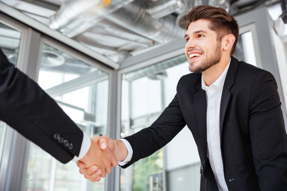 Smiling male college student shaking hands with someone out of frame