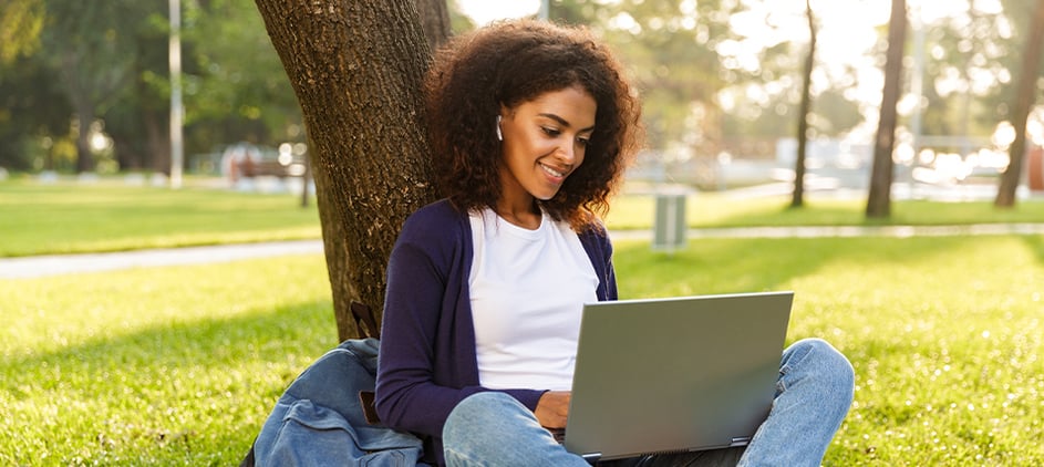 High school student sitting against a tree with laptop