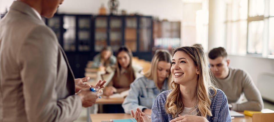 student in college class, smiling at professor