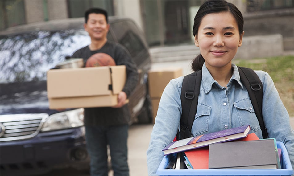 College student walking into college dorm carrying a box of books.