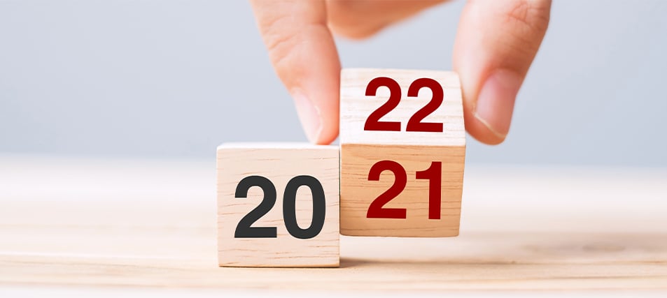 Close-up of wooden blocks. A hand reaches down and flips over the block displaying the year 2021  to display the year 2022.